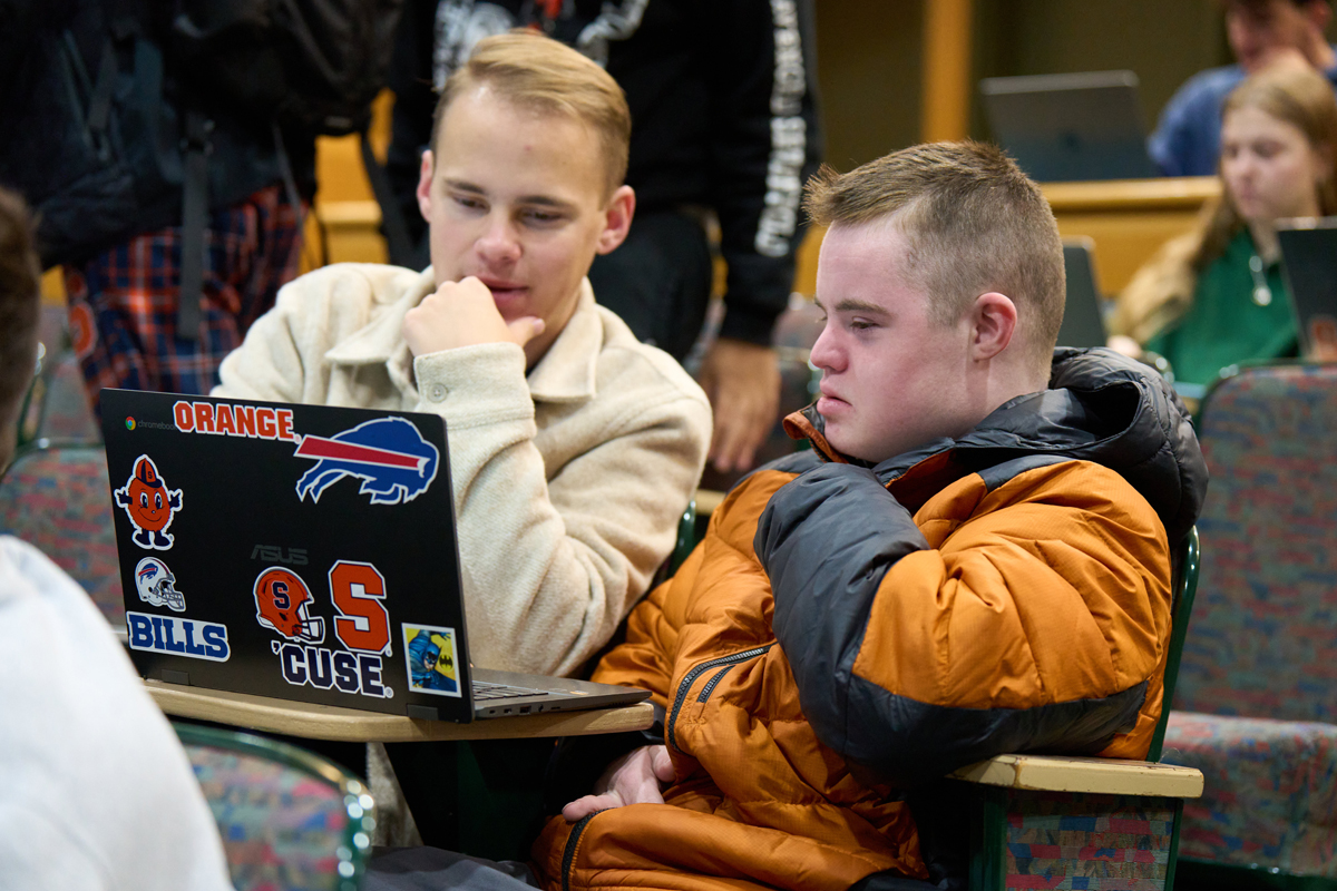 Two brothers look at a laptop while seated for a class in the Falk College.