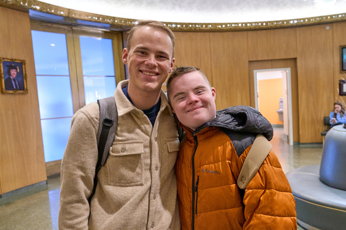 Two brothers embrace while posing for a headshot inside the Falk College.