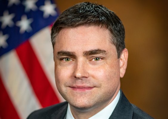 A man poses for a headshot with an American flag in the background.