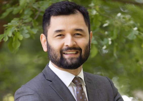 A man smiles while posing for a headshot outdoors.