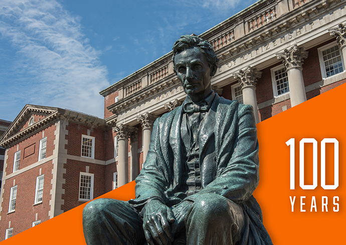 Bronze statue of Abraham Lincoln seated in front of the Maxwell Hall, with a banner saying "100 Years" on the right side.