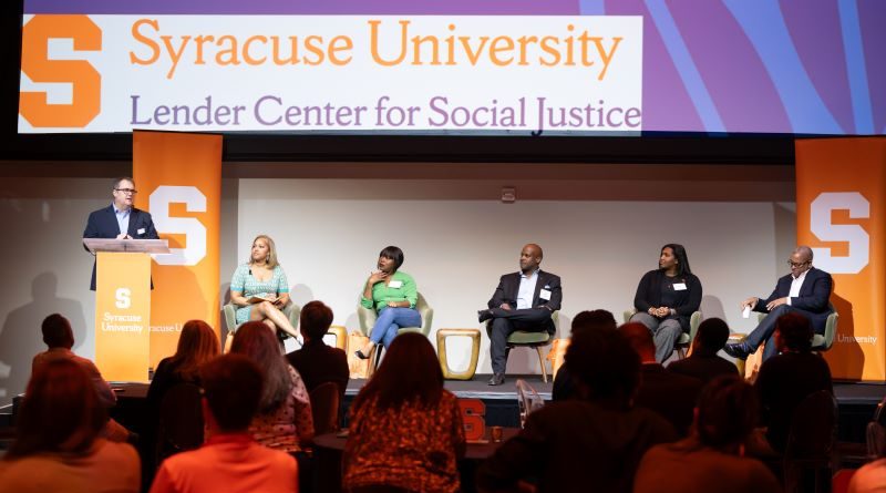 panel of five people are introduced to the audience at a large gathering