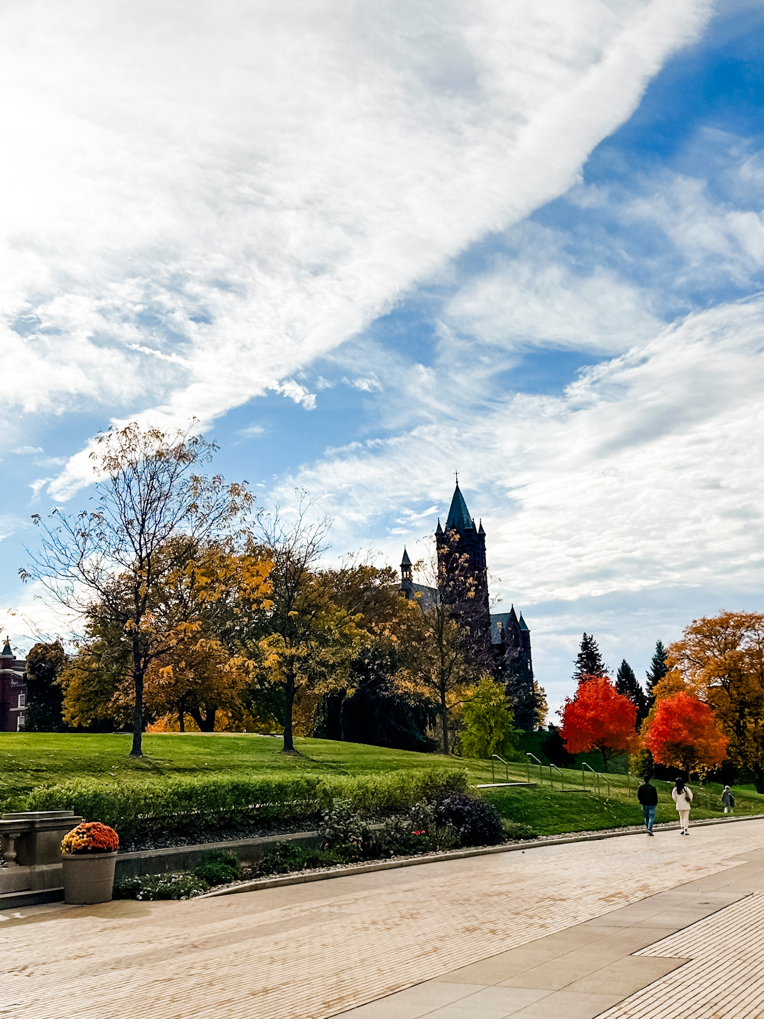 Beautiful autumn day on the Syracuse University campus with colorful trees, a blue sky with clouds, and people walking.