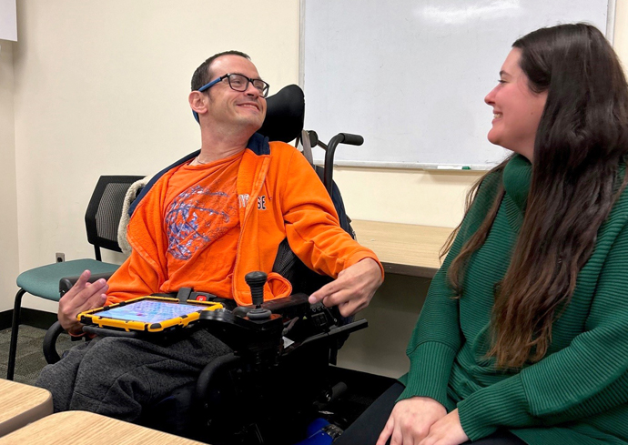 Two people engage in conversation using Alternative Augmentative Communication, which helps individuals express themselves.