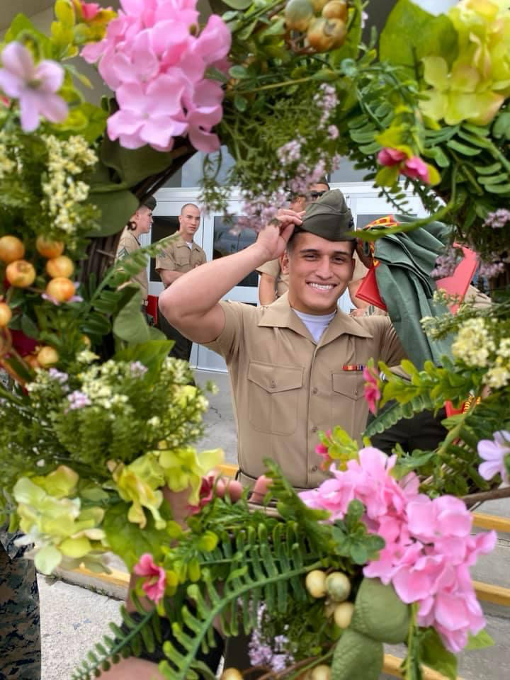 A person in a military uniform saluting, framed by a colorful wreath of flowers.