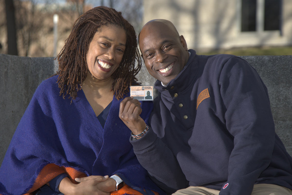 A wife and husband pose for a photo while sitting on a bench at Syracuse University.