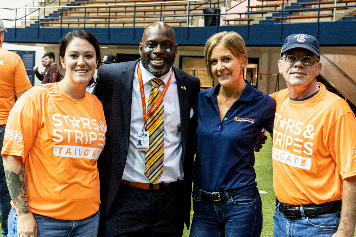 Four people smile while posing for a group photo at a tailgate.