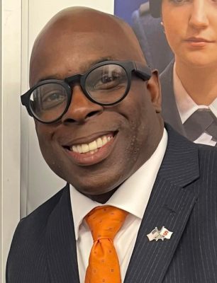 A man smiles for a headshot while wearing an Orange tie.