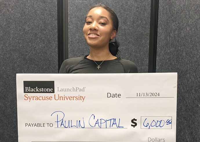 A woman smiles while holding up a check.