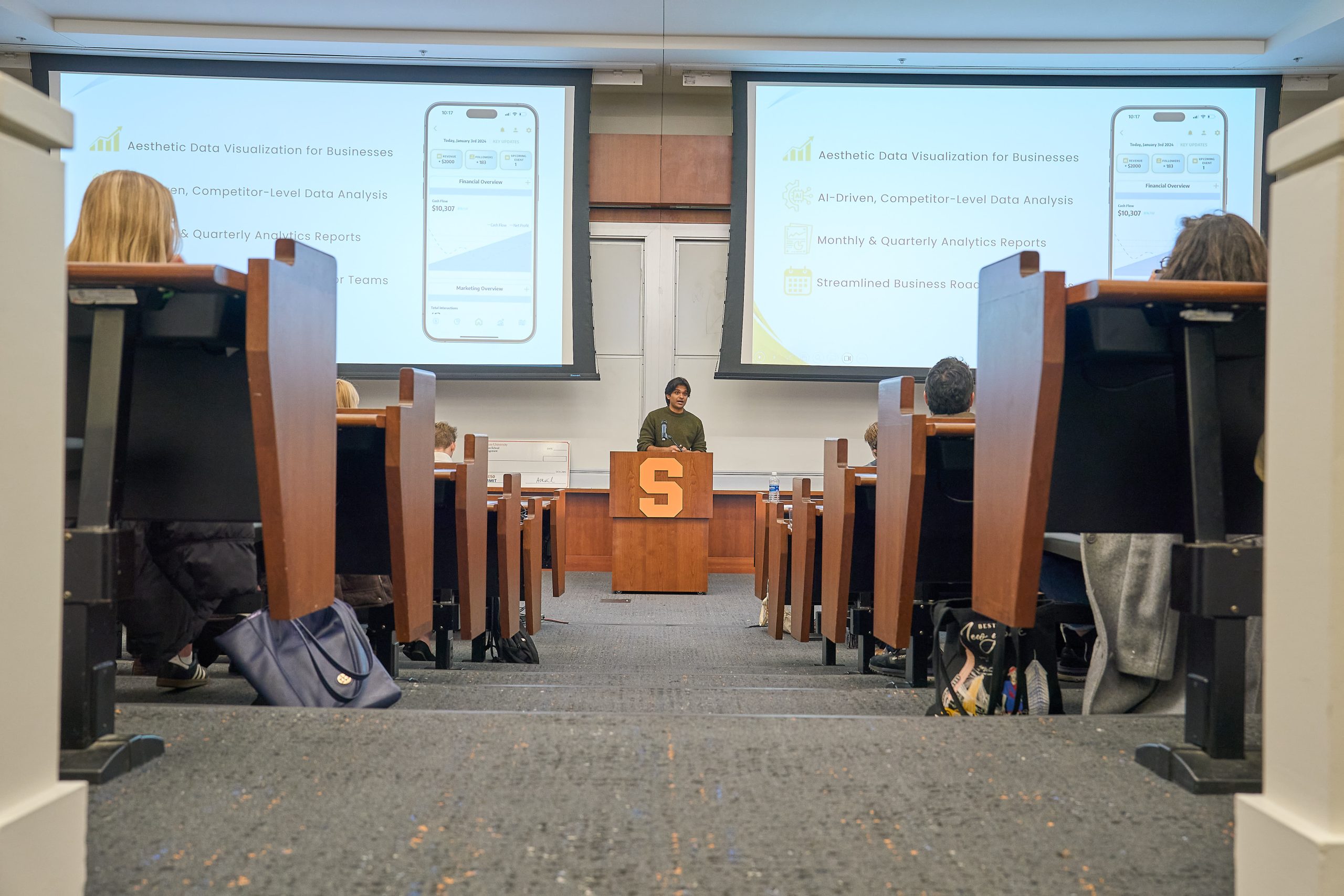 A person presenting at a lecture hall with students seated facing the speaker.