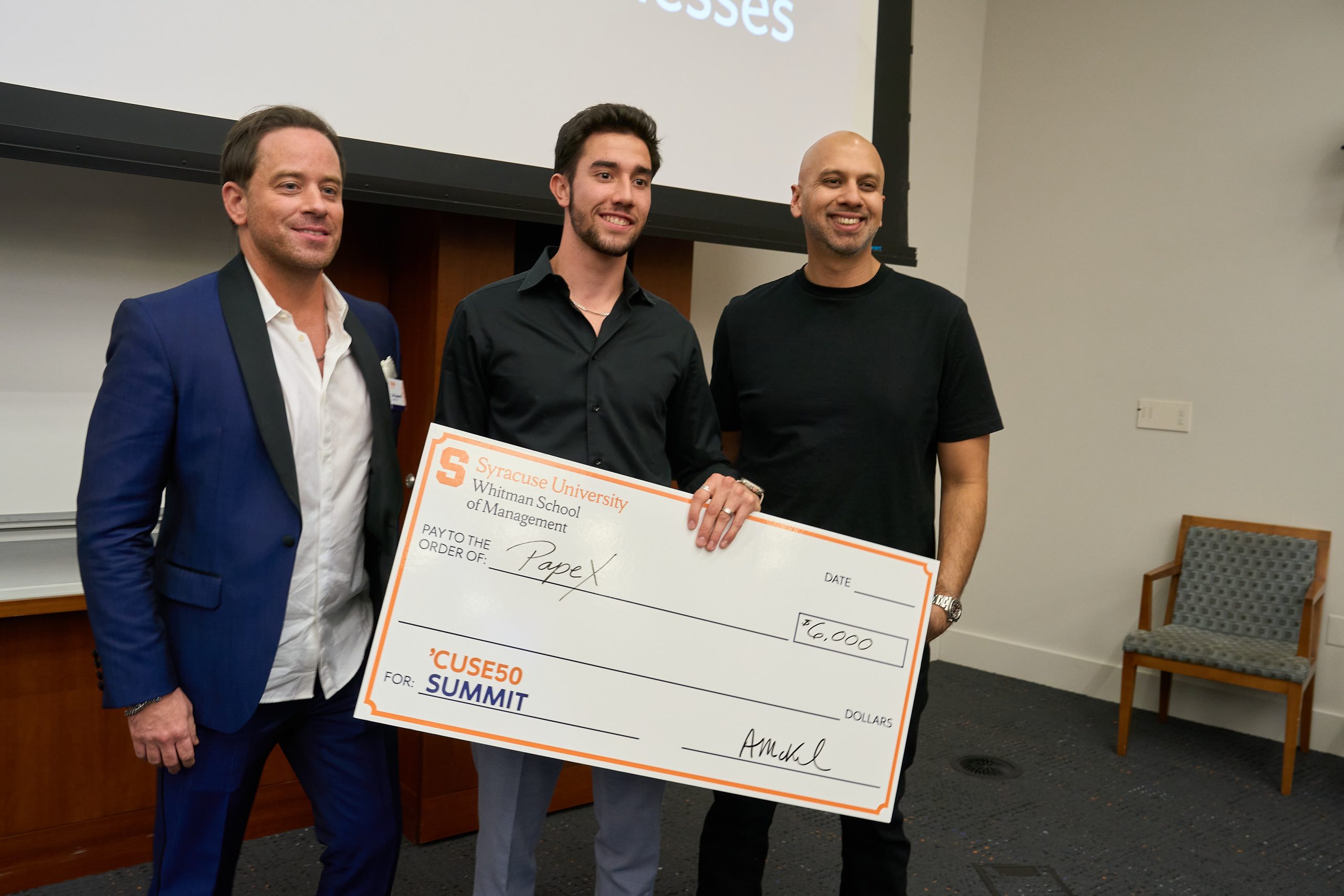 Three individuals posing with a large ceremonial check at the 'Cuse for Summit event at Syracuse University Whitman School of Management.