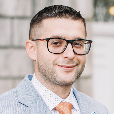 A man smiles while posing for a headshot while standing outside.