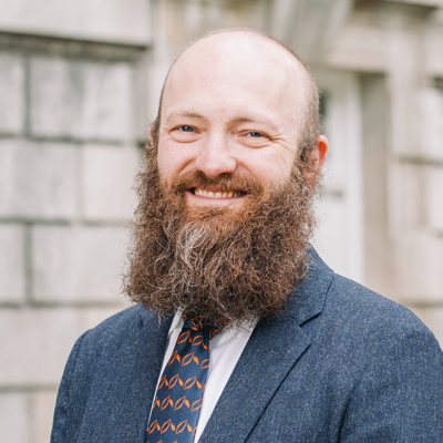 A man smiles for a headshot while standing outside.