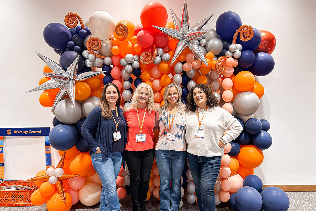 Four alumni smile and pose for a photo at Orange Central.