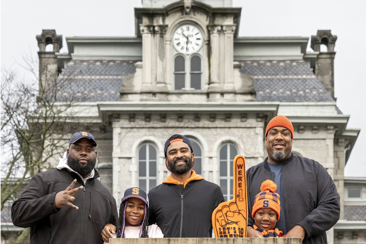 People wearing Syracuse University gear pose for a photo in front of the Hall of Languages.