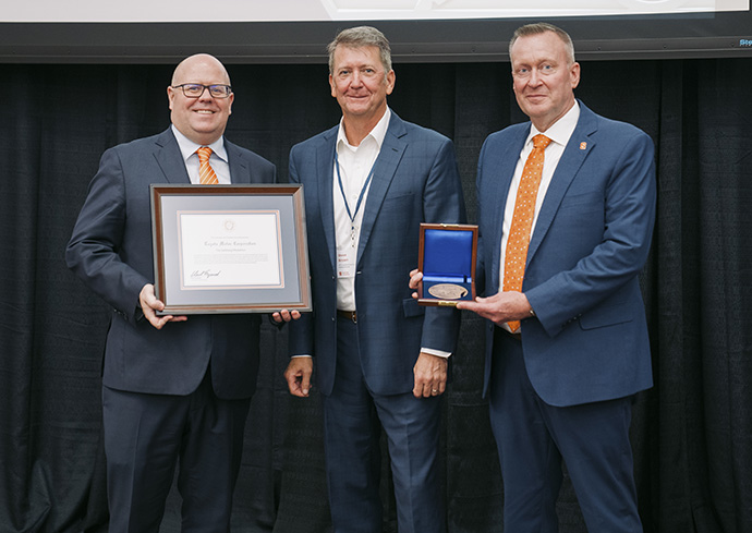 three people standing with one person holding certificate and another person holding award