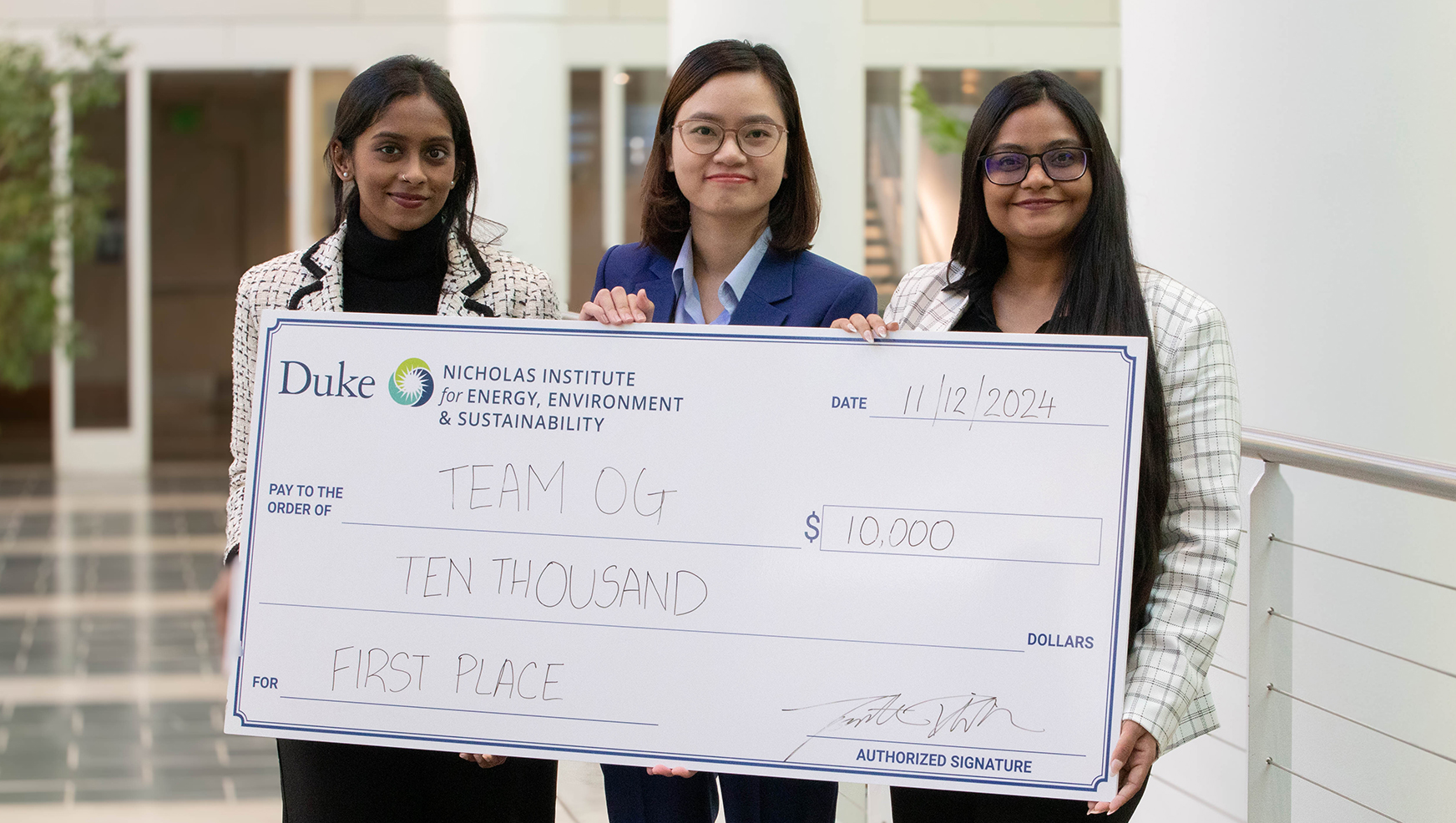 Three people standing and holding a large check