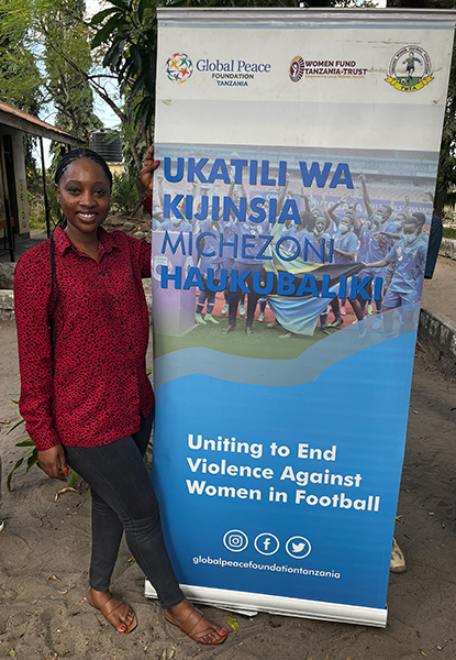 A woman stands and poses for a photo next to a poster reading uniting to end violence against women in football.