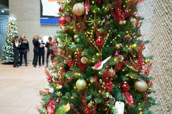 Decorated Christmas tree with colorful baubles and lights, with people standing in the background in a lobby setting.