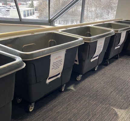 Four large grey bins with paper taped to the outside of them for donations to be collected