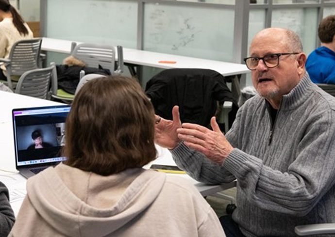 An alumnus sits down and works with students.