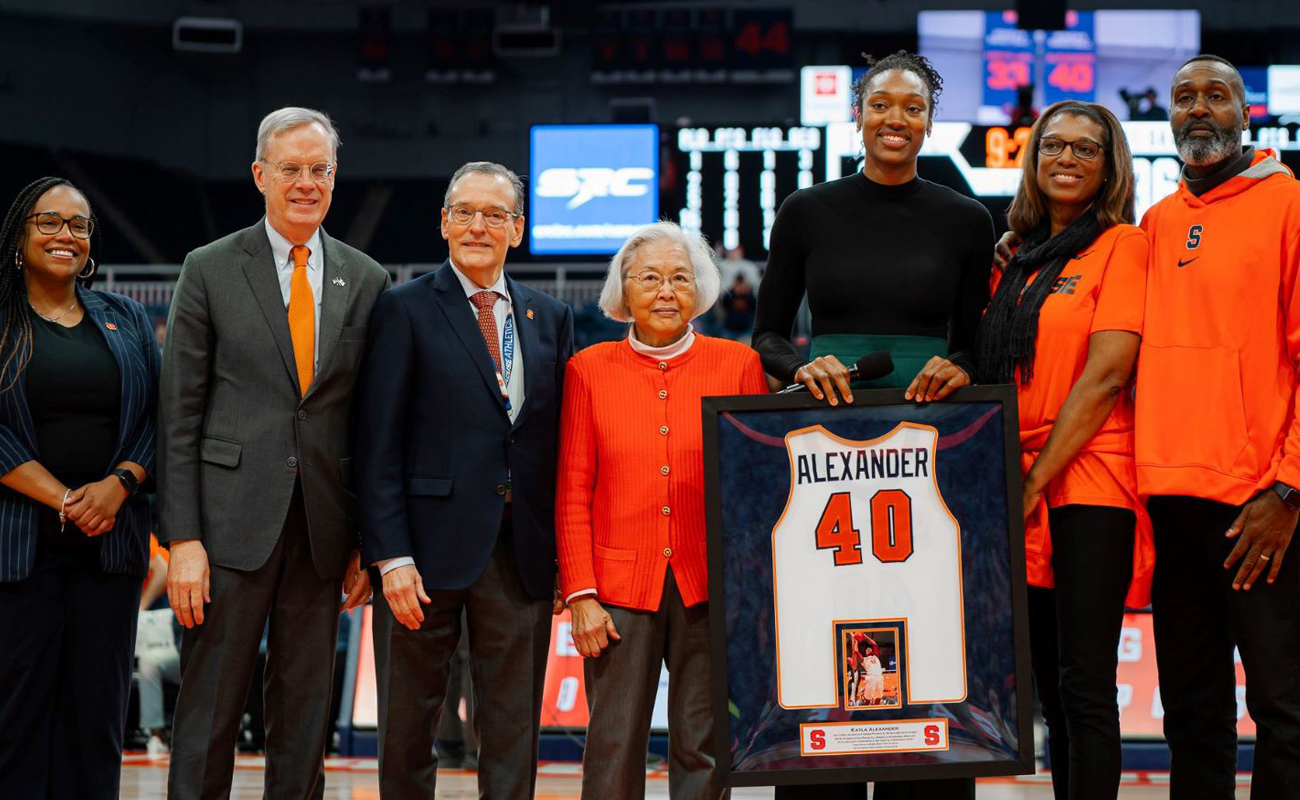 A woman has her jersey retired by the Syracuse University women's basketball team while surrounded by friends, family and University leadership.