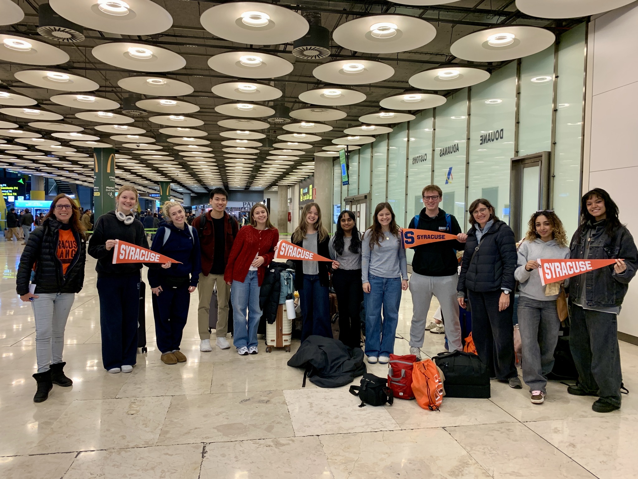 Group of people holding Syracuse University scarves in an airport terminal.