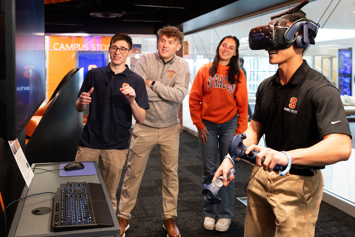 A student uses a virtual reality machine while students cheer him on.