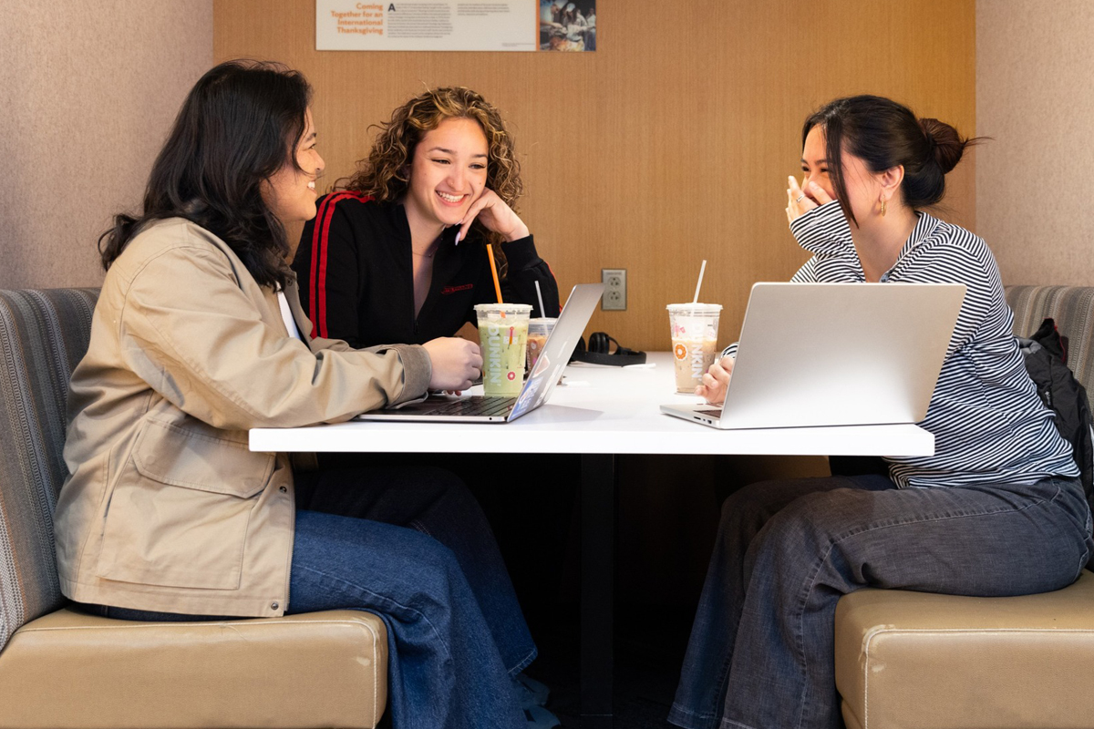 Three students sit around a table and chat on the first day of classes.