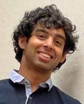 headshot of a person with dark curly hair wearing a button up shirt