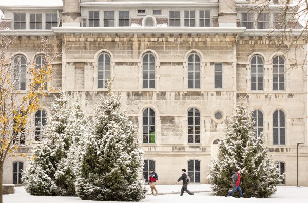 Students walking past a building on a snow-covered day on the Syracuse University campus.