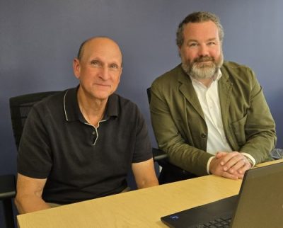 two men at a desk with a laptop looking ahead