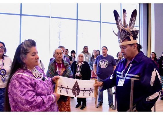 Members of the Native American community gathered together looking at a textile