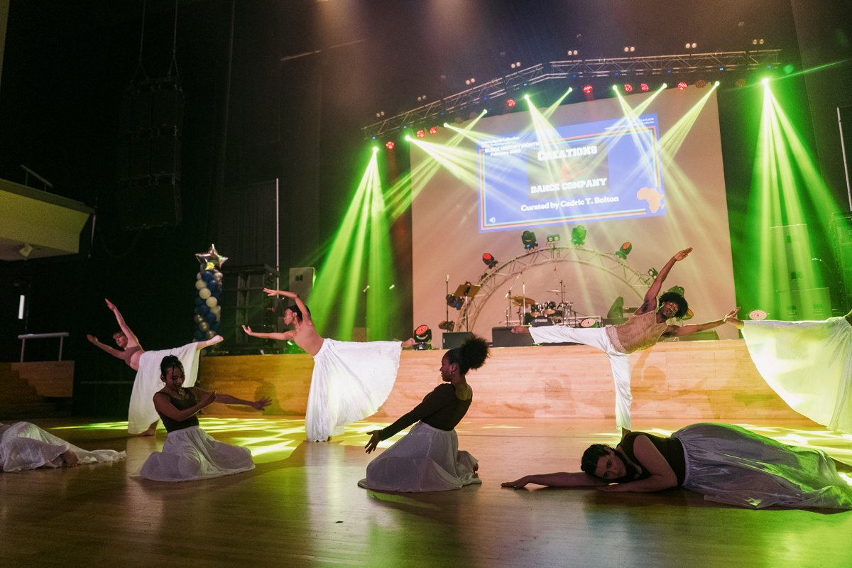 Dancers performing on a stage with lights in the background.