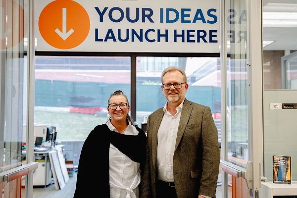 two people standing in front of an office with a sign above them that reads Your Ideas Launch Here