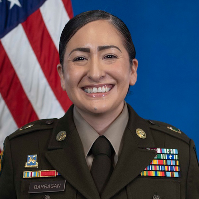 A military officer smiles while posing for a headshot in military uniform with the U.S. flag in the background.