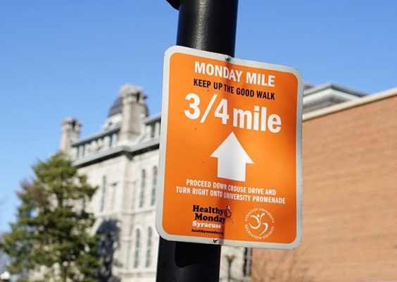 an orange sign with white print attached to a lamp post with the words Monday Mile Keep Up The Good Walk 3/4 Mile