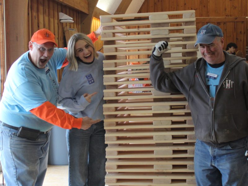 Three people smile while posing with a bed they made.