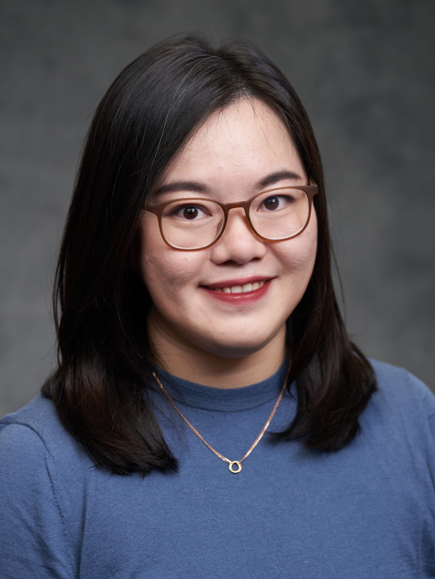 The image shows a person with long, dark hair against a gray background.