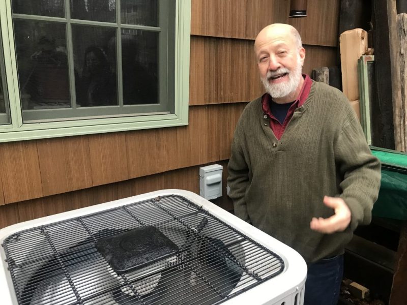 Ian Shapiro stands besides a heat pump outside of a house