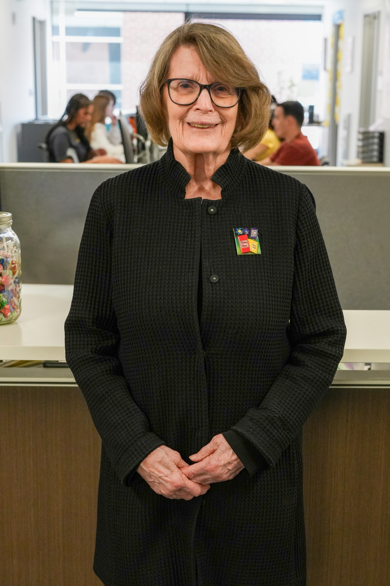 Pamela Kirwin Heintz stands in her office with students behind her.