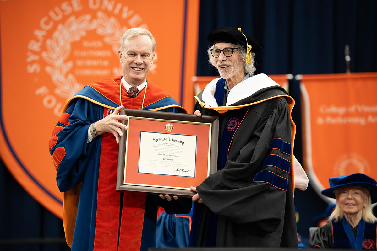 Two individuals in academic regalia, Chancellor Kent Syverud and Bob Mankoff, hold a framed diploma from Syracuse University.