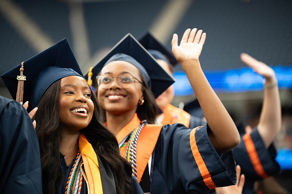 A group of graduates wearing caps and gowns, with some raising their hands.