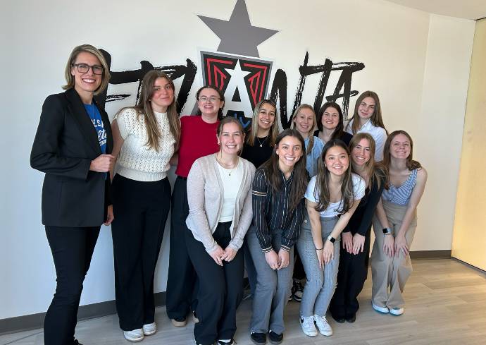 A group of twelve people posing for a photo in front of a mural that features the word 'ATLANTA' in large, stylized letters, along with a prominent star and an 'A' symbol. The individuals are dressed in casual to business-casual clothing, with some standing and others kneeling.