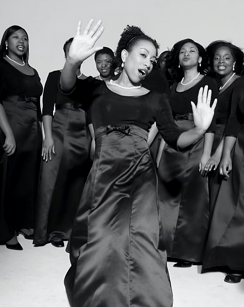 a person in a gown singing in front of a row of others in gowns singing