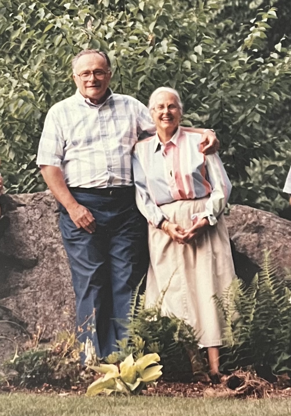 two people standing next to each other in front of rock and bushes
