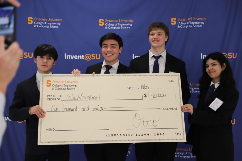 Wash Sentinel team members hold a large $4,000 check in front of a Syracuse University 'Invent@SU' banner.