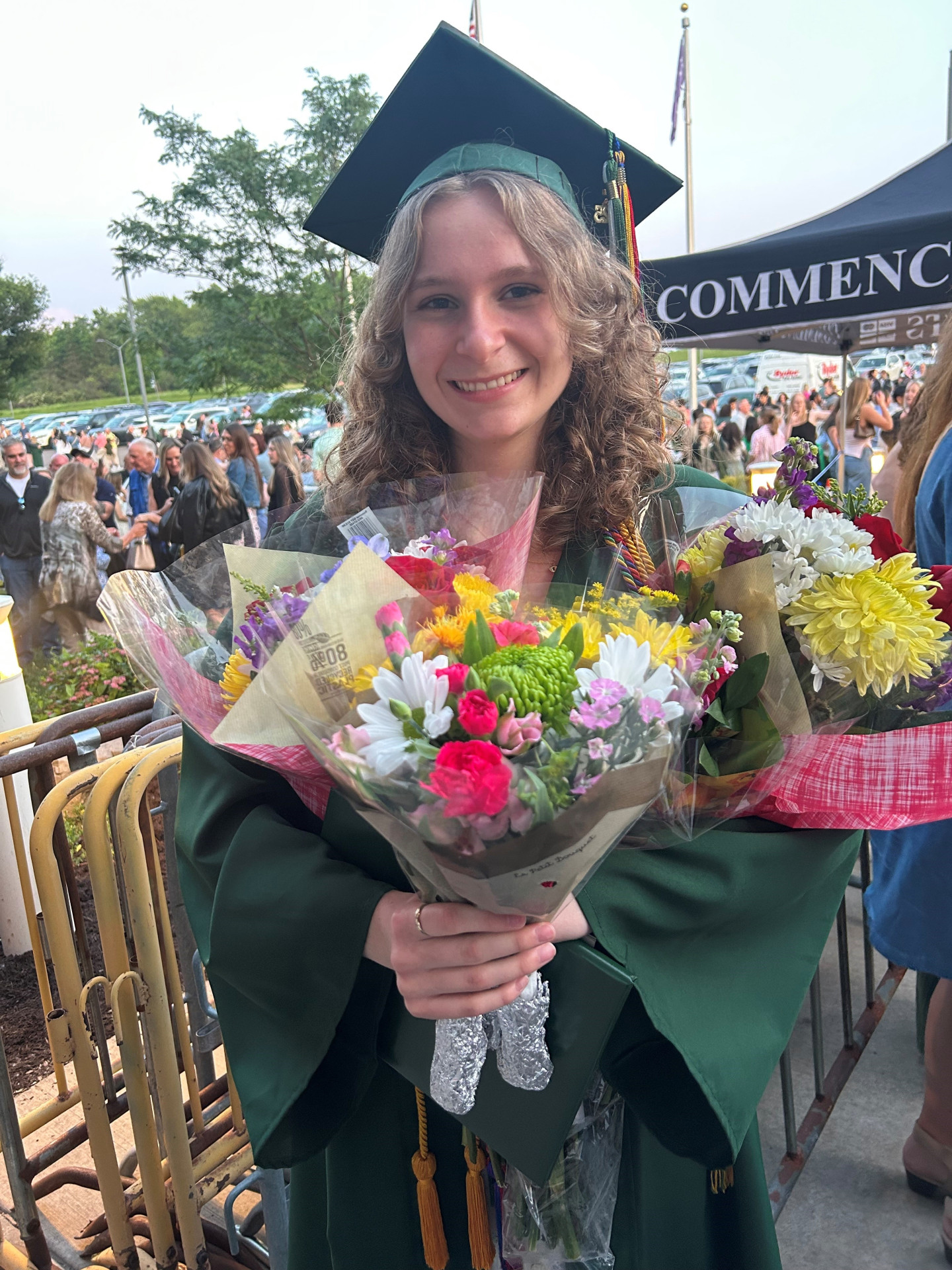 Emilia Cappers in graduating cap and gown and holding bouquets of flowers