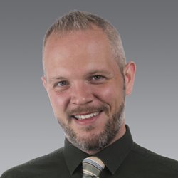 Person in a dark green shirt and striped tie against a gray gradient background