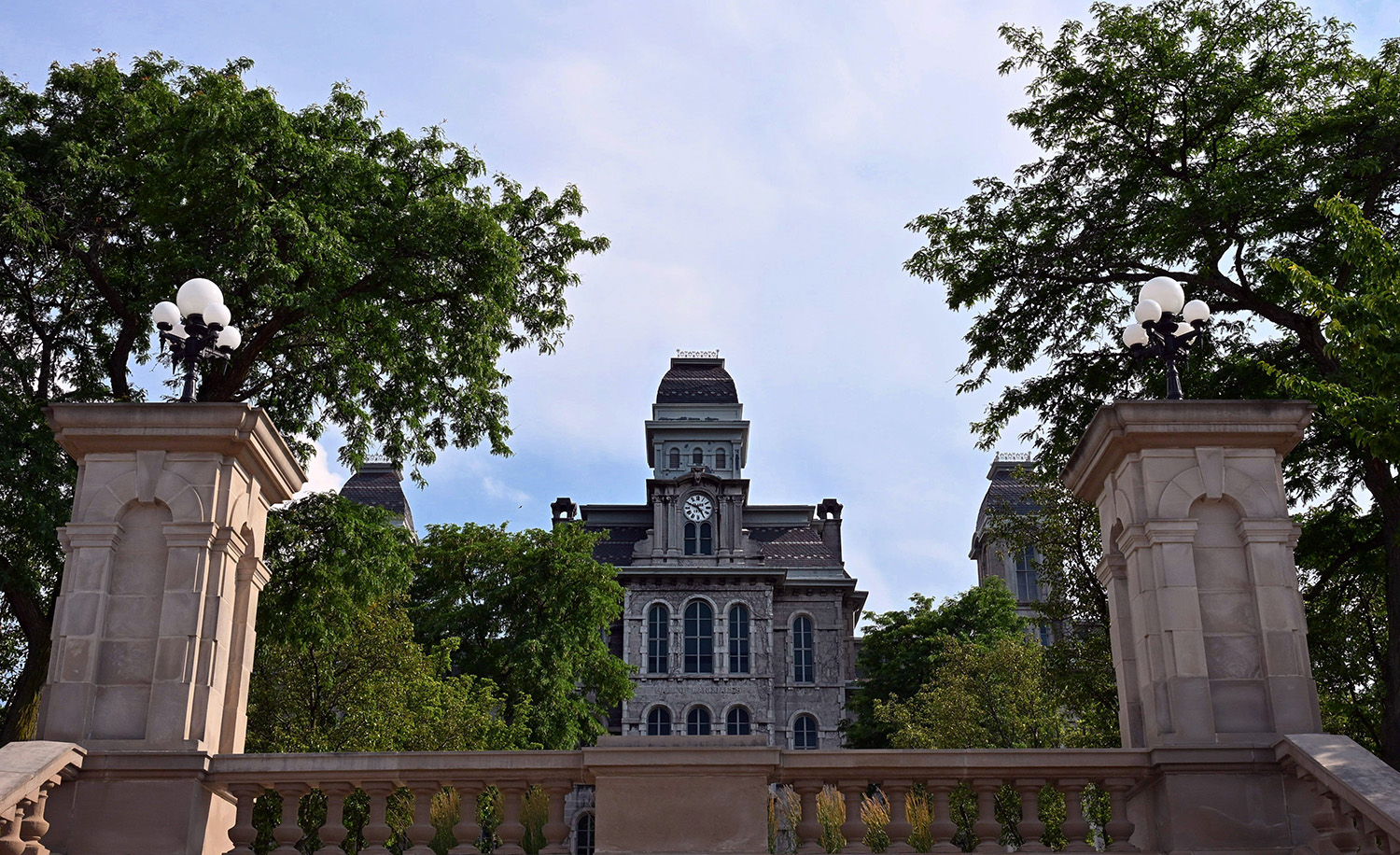 Historic Hall of Languages building framed by stone pillars and street lamps, surrounded by green trees under a clear blue sky.